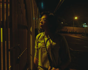 Young man standing by gate at night