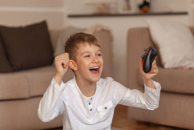 Happy boy holding video game remote control in living room at home 