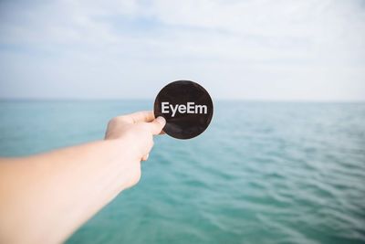 Close-up of hand holding text at beach against sky