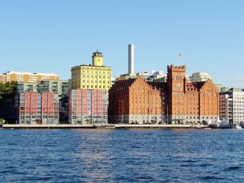 Sea by cityscape against clear blue sky