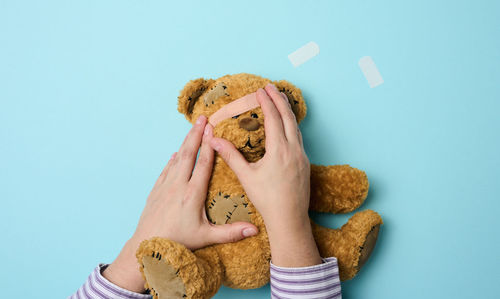 Female hand holds a brown teddy bear and glues a medical adhesive plaster on a blue 