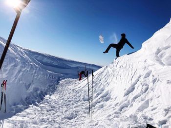 Low angle view of man kicking snow against blue sky during sunny day