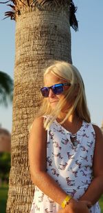 Girl wearing sunglasses standing by tree trunk