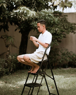 Side view of young man sitting on chair in yard