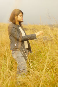 Young woman standing on grassy field against sky