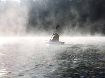 Man rowing boat in sea against sky