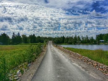 Road passing through field against cloudy sky