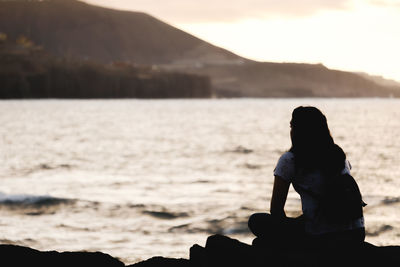 Rear view of silhouette man sitting on beach