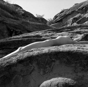 Shirtless woman lying on rock against sky