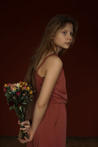 Portrait of young woman holding rose against black background