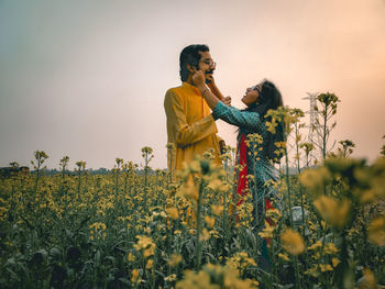 Young woman standing on yellow flowering plants on field against sky