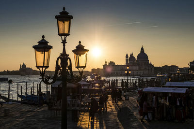 Gas light and people on promenade by grand canal with santa maria della salute during sunset