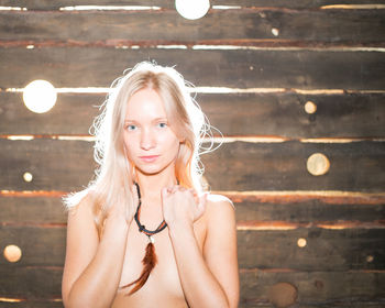 Portrait of sensuous young woman covering breasts with hands against wooden wall