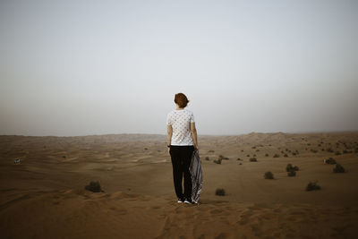 Rear view of woman standing on sand in desert