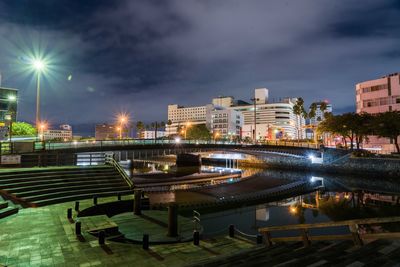 Illuminated buildings by river against sky in city at night