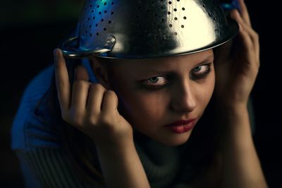 Close-up portrait of serious teenage girl with colander against black background