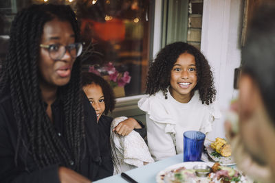 Curious sisters sitting with mother while having food at restaurant