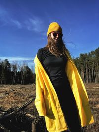 Woman standing by yellow umbrella on field against sky