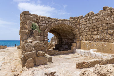 View of old ruin by sea against cloudy sky