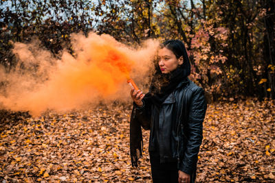 Young woman holding distress flare while standing in forest during autumn