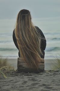Young woman with long hair looking at sea shore against sky.