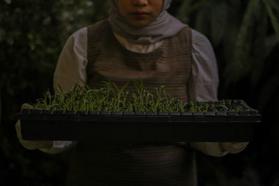 Midsection of man holding camera while standing against plants