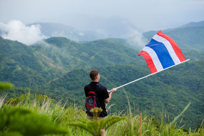 Man with thai flag standing on field against mountains