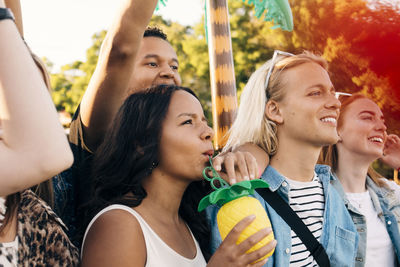 Woman having drink while standing with smiling fans in music festival