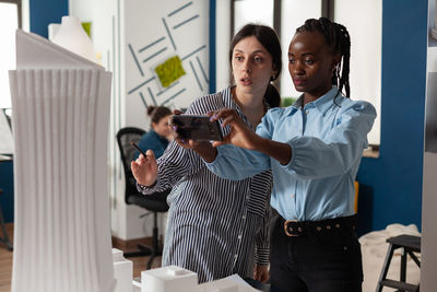 Portrait of young woman using mobile phone while standing in office