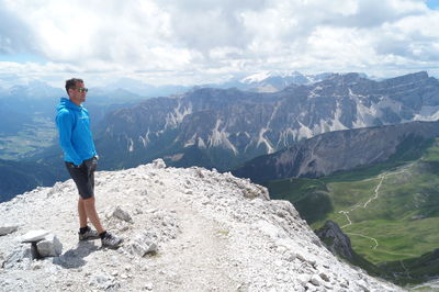 Full length of man standing on peak against rocky mountains and cloudy sky