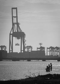 Silhouette people fishing in sea against construction site