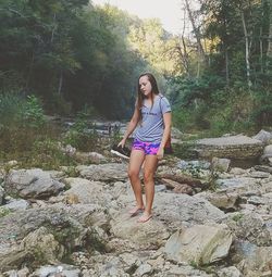 Young woman standing on rock against trees