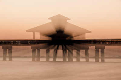 Silhouette built structure by sea against sky during sunset