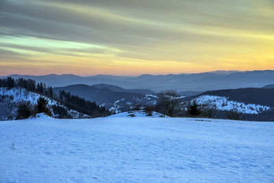 Scenic view of snow covered field against sky at sunset