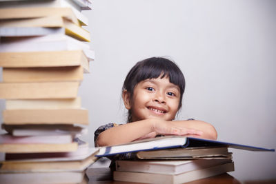 Portrait of smiling girl sitting by stacked books