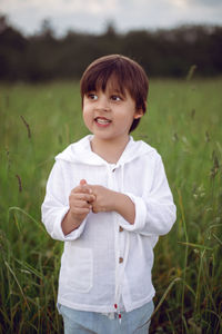 Boy child in a green field in summer in a white shirt with a hood made  linen in shorts and sandals