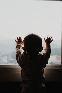 Rear view of boy looking through window