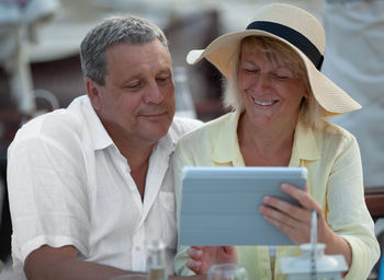 Smiling mature woman showing digital tablet to man at sidewalk cafe