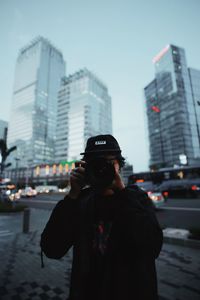 Man photographing while standing on city street against sky