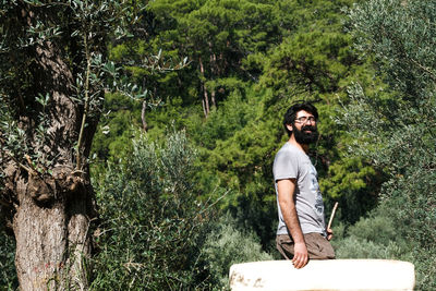 Portrait of young man standing against trees in forest