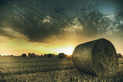 Hay bales on field against sky during sunset