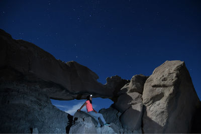 Rear view of person on rock against sky at night