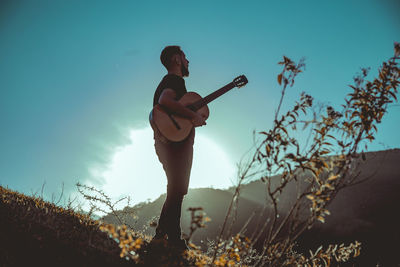 Man standing with guitar against sky