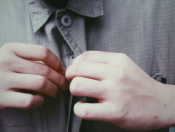 Midsection of man buttoning shirt