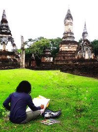 Rear view of man sitting outside temple against building