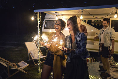 Happy friends burning sparklers during camping