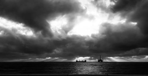 Silhouette ship sailing in sea against dramatic sky
