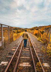 Rear view of person standing on railroad tracks against sky