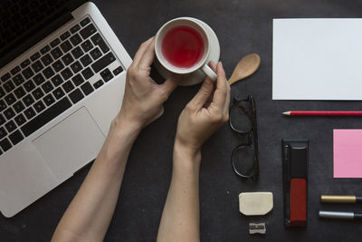 Cropped hands of woman holding coffee cup on desk