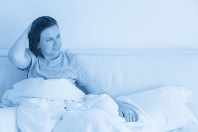 Young woman sitting on bed at home